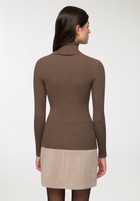 Maglione a collo alto marrone a coste con maniche lunghe, abbinato a una mini gonna in suede beige chiaro. Tessuto liscio, design aderente.