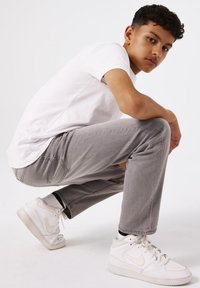 Jeans grises de corte relajado, combinados con una camiseta blanca de manga corta y zapatillas blancas. Tejido suave; sin patrones ni logotipos visibles.