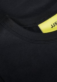 Zwarte katoenen t-shirt met een geribbelde ronde hals en een gele label met zwarte tekst. Zachte stof en eenvoudig ontwerp.