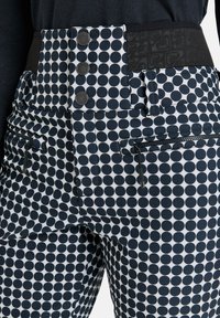 Niebieskie i białe spodnie w kropki z wysokim czarnym pasem, który posiada trzy guziki oraz kieszenie zapinane na zamek z przodu.