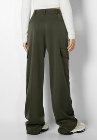 Olivgröna cargobyxor med hög midja, sidofickor och vida ben. Tillverkade av ett glatt tyg med en subtil lyster.