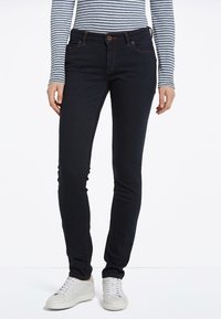 Jeans ajustados de un azul oscuro con una textura suave, que cuentan con un diseño clásico de cinco bolsillos y costuras en contraste, combinados con zapatillas blancas.