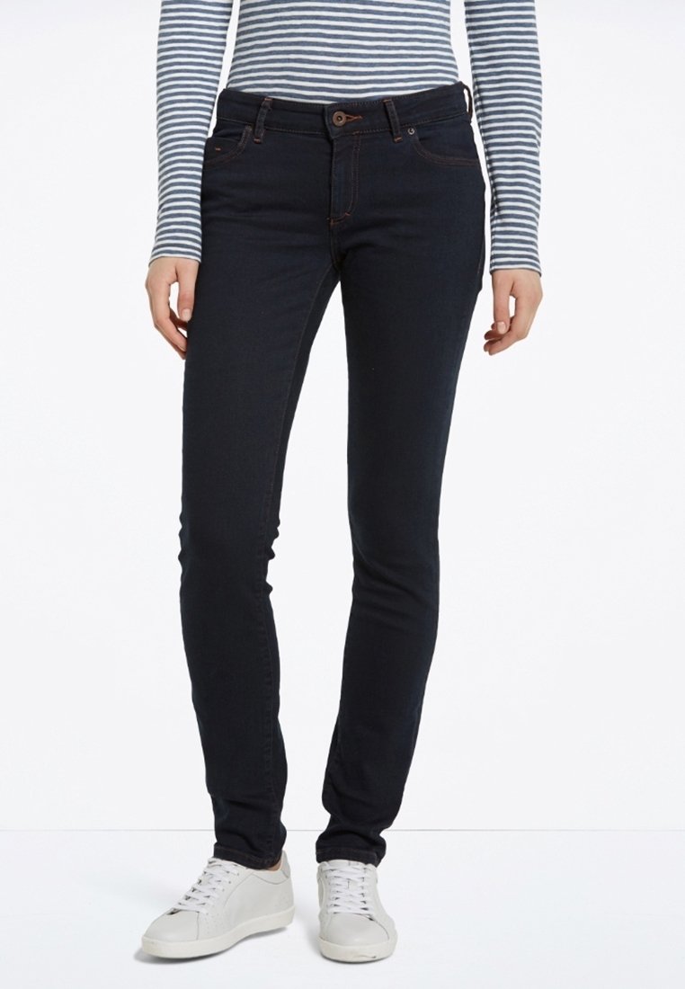 Jeans ajustados de un azul oscuro con una textura suave, que cuentan con un diseño clásico de cinco bolsillos y costuras en contraste, combinados con zapatillas blancas.