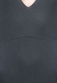 Σκούρο γκρι κορυφή από ριγωτό ύφασμα με ντεκολτέ σε σχήμα V, με διακριτική οριζόντια ραφή στο πάνω μέρος. Λείο υλικό και εφαρμοστή σχεδίαση.