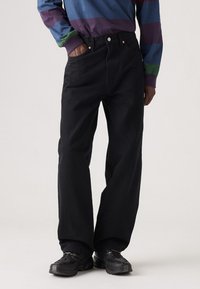 Jeans neri a gamba larga in denim, con vita alta, tasche frontali e cuciture a contrasto. Abbinati a una camicia a maniche lunghe multicolore.