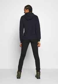 Granatowy hoodie z kapturem na sznurki, z prążkowanymi mankietami i dołem, zestawiony z czarnymi spodniami i zielonymibutami. Gładka tekstura materiału, luźny krój.