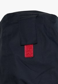 Tessuto blu navy con finitura testurizzata, dotato di un patch rettangolare in Velcro rosso nella parte superiore e una patta per la chiusura.