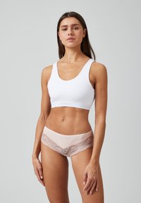 Witte katoenen cropped tanktop met brede straps, gecombineerd met lichtroze ondergoed met kantafwerking en een floral patroon op het kant.