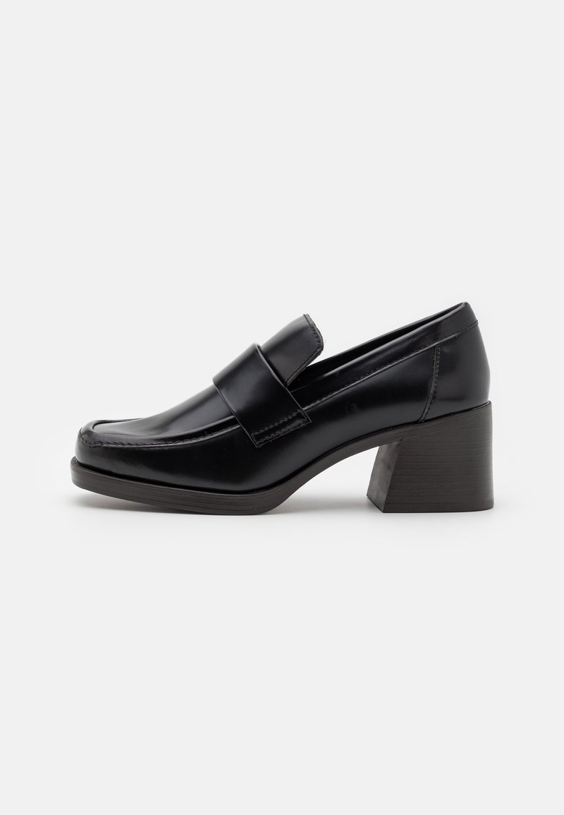 Mocassin femme en cuir noir avec talon bloc et détail de bride sur le dessus, présenté en profil sur fond blanc.
