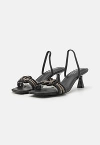Musta slingback-sandaalit neliömäisellä varpaalla, jossa on kudottu nauhadesign ja kiiltävä korko. Valmistettu sileästä materiaalista, jossa on teksturoitu yksityiskohta.