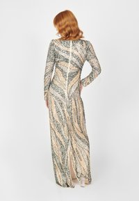 Robe longue moulante en sequins argentés, dorés et verts avec des motifs en vagues, dotée de manches longues et d'une fermeture éclair dans le dos, avec un détail de fente haute.