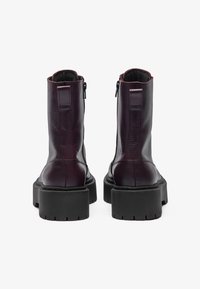 Bottines en cuir bordeaux avec fermeture à glissière, semelle extérieure noire épaisse et talon robuste ; texture lisse avec un minimum de détails.
