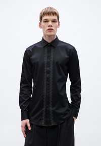 Fekete ing sima anyagból, finoman texturált függőleges panellel az elején; klasszikus gallérral és hosszú ujjal.