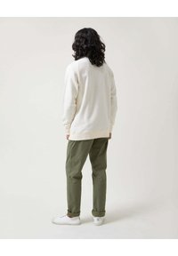 Sudadera de algodón color crema con puños acanalados, combinada con pantalones de algodón verde oliva y zapatillas blancas, vista desde la espalda.