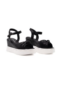 Sandali wedge neri in pelle liscia, con design annodato e piattaforma in gomma bianca con dettagli del logo. Cinghia alla caviglia regolabile.