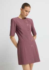 Vestido ajustado de manga corta en un profundo color malva, con cinco grandes botones circulares, dos bolsillos laterales y una silueta limpia y estructurada.