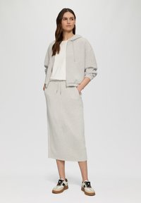 Helles graues Hoodie mit Reißverschluss, gerippten Bündchen und Seitentaschen, kombiniert mit einem passenden Midirock und mehrfarbigen Sportschuhen.