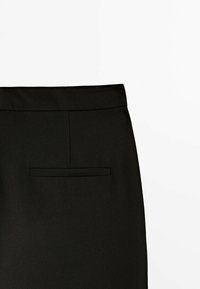 Jupe noire présentant une texture lisse, un design sur mesure, une coupe droite, et une seule poche arrière avec un rabat rectangulaire.