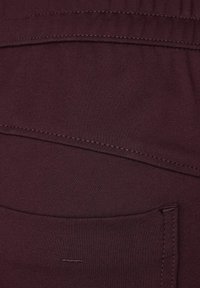 Tumma burgundiväri kangas, jossa on sileä rakenne, jossa on sauman ja taskun yksityiskohtia. Materiaali on joustava, mikä lisää mukavuutta ja sovitusta.