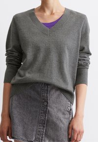 Pull en tricot gris à col en V avec des poignets côtelés, superposé sur une chemise violette. Associé à une jupe en denim grise, affichant un look décontracté.