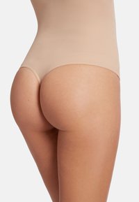 Naadloos bodysuit van huidkleurige stof met een gladde textuur en lage taille, die de natuurlijke vorm en contouren benadrukt.