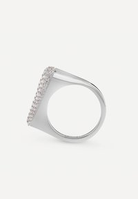 Srebrny pierścionek z płaską powierzchnią ozdobioną licznymi małymi przejrzystymi kamieniami, zwężającą się obrączką, nowoczesny geometrystyczny design.