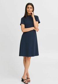 Marinblå klänning med kort ärm, avslappnad passform, slät tyg, rund halsringning och knä-lång design. Matchad med svarta remsandaler.