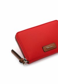 Rotes Reißverschluss-Wallet aus glattem synthetischen Material mit braunen Lederakzenten und einem strukturierten Logopatch, ausgestattet mit einem dekorativen Reißverschlussanhänger.
