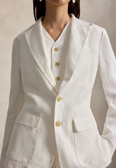 Γυναίκα με εκρού ραμμένο σακάκι πάνω από πουκάμισο με κουμπιά, με τσέπες με καπάκι και γιακά με εγκοπή.