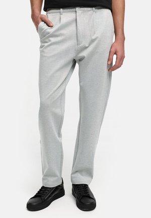 Lichtgrijze op maat gemaakte broek van zachte stof, met zijzakken, voorplooien en een relaxte pasvorm, gecombineerd met zwarte sneakers.