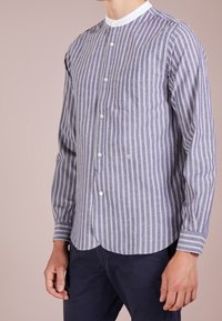 Camicia a maniche lunghe a righe in navy e bianco, con colletto rotondo, bottoni frontali e taschino sul petto. Tessuto morbido con una vestibilità rilassata.