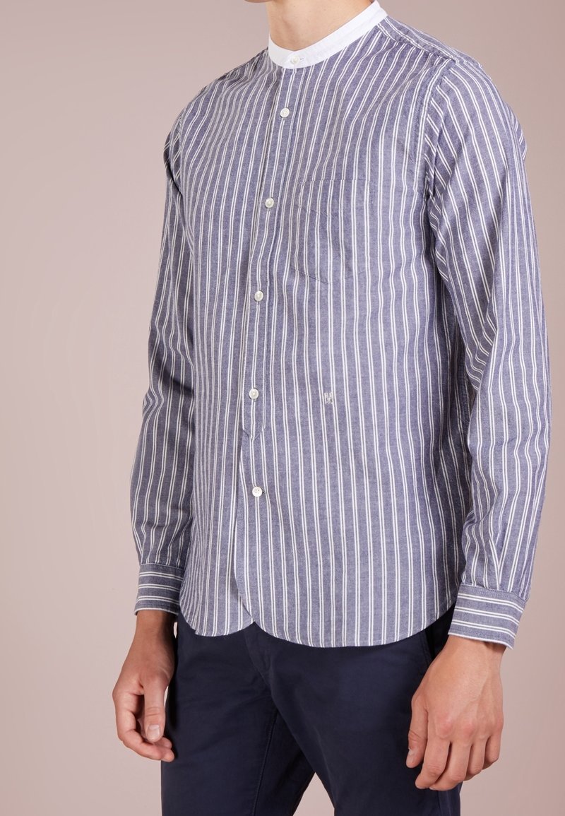 Camicia a maniche lunghe a righe in navy e bianco, con colletto rotondo, bottoni frontali e taschino sul petto. Tessuto morbido con una vestibilità rilassata.