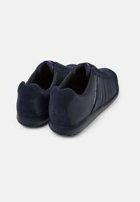 Tenisi cu talpă joasă de culoare bleu marin, prezentând o combinație de texturi netede și din suede, detalii subtile cu dungi și un toc rotunjit pentru confort.