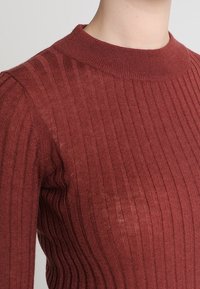 Bordeaux ribgebreide pullover met een ronde hals, textuurstof en gestructureerde pasvorm, die verticale lijnen door het gehele kledingstuk benadrukt.