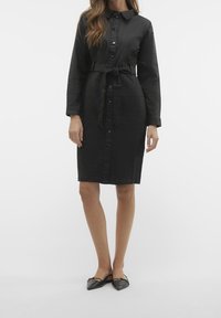 Czarna sukienka na guziki z gładkiego materiału, z długimi rękawami, paskiem w talii do związania i długością do kolan. Prosty, elegancki design.