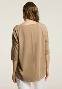 Luźna beżowa bluzka z dekoltem typu łódka i rękawami o długości trzech czwartej. Wykonana z miękkiego materiału o gładkiej fakturze, z detalem szwu z tyłu.