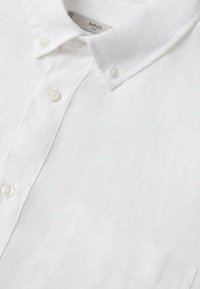 Chemise blanche pour homme à boutons avec col boutonné et poche poitrine, confectionnée dans un tissu texturé.