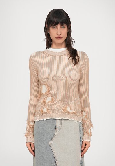 Pull en maille côtelée pêche clair avec détails effilochés, doté d'un col rond et de manches longues, superposé sur une jupe en jean grise.