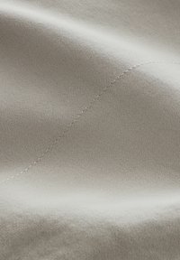Tejido beige claro con una textura suave y un sutil brillo. Presenta una delicada canaladura y un detalle de costura en contraste.