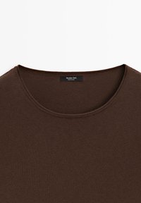 Pull marron à col rond avec une texture en maille fine et une étiquette noire à l'intérieur du col indiquant la marque et le pays de fabrication.