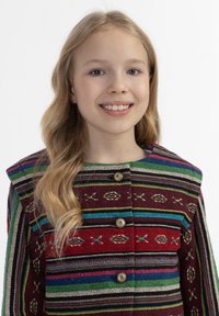 Daugiaspalvė megzta striukė su raudonomis, žaliomis ir mėlynomis juostelėmis. Yra dekoratyvūs mygtukai ir sudėtingi geltoni bei balti raštai.