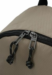 Mochila beige con un patrón cuadrado texturizado, cremallera negra con dos tiradores y detalles en cordón negro para un cierre seguro.