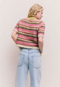 Rövid ujjú, rövidített pulóver, amely színes csíkokat tartalmaz rózsaszín, zöld és fekete színekben. Puha tapintású, bordázott nyak- és szegély részletekkel. Farmernadrág.
