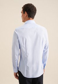 Camicia azzurra chiara con colletto aperto, maniche lunghe, polsini abbottonati e orlo curvo. Tessuto liscio con un design pulito.