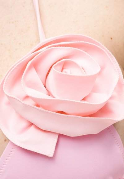 Κοντινή λήψη λεπτομέρειας από ροζ υφασμάτινο τριαντάφυλλο σε ρούχο ανοιχτό ροζ χρώματος σε ανοιχτόχρωμο δέρμα.