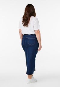 Temno modra denim krila s ravnim krojem, dolžine do meč, ter zadnjimi žepi. V kombinaciji z belo majico in belimi športnimi čevlji.
