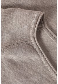 Hellbrauner Strickstoff mit sichtbaren Nähten und glatter Textur. Verfügt über einen runden Halsausschnitt und Nahtdetails entlang der Kanten.