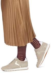 Beige Wildledersneaker mit weißen Akzenten, ausgestattet mit einem strukturierten Obermaterial, Schnürverschluss und Gumminsohle, kombiniert mit gerippten bordeauxroten und cremefarbenen gestreiften Socken sowie einem plissierten hellbraunen Rock.