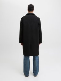 Μαύρο παλτό με κοψίματα στον γιακά, μεσαίου μήκους σχέδιο, συνδυασμένο με ανοιχτό μπλε φαρδιά τζιν. Λείος υφασμάτινος σχεδιασμός, μινιμαλιστικό στυλ.