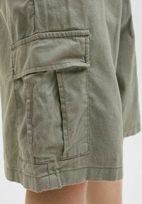 Zelene cargo kratke hlače iz lahkega materiala imajo več žepov z poklopci in opletenimi detajli, zaključene z robom brez obdelave.